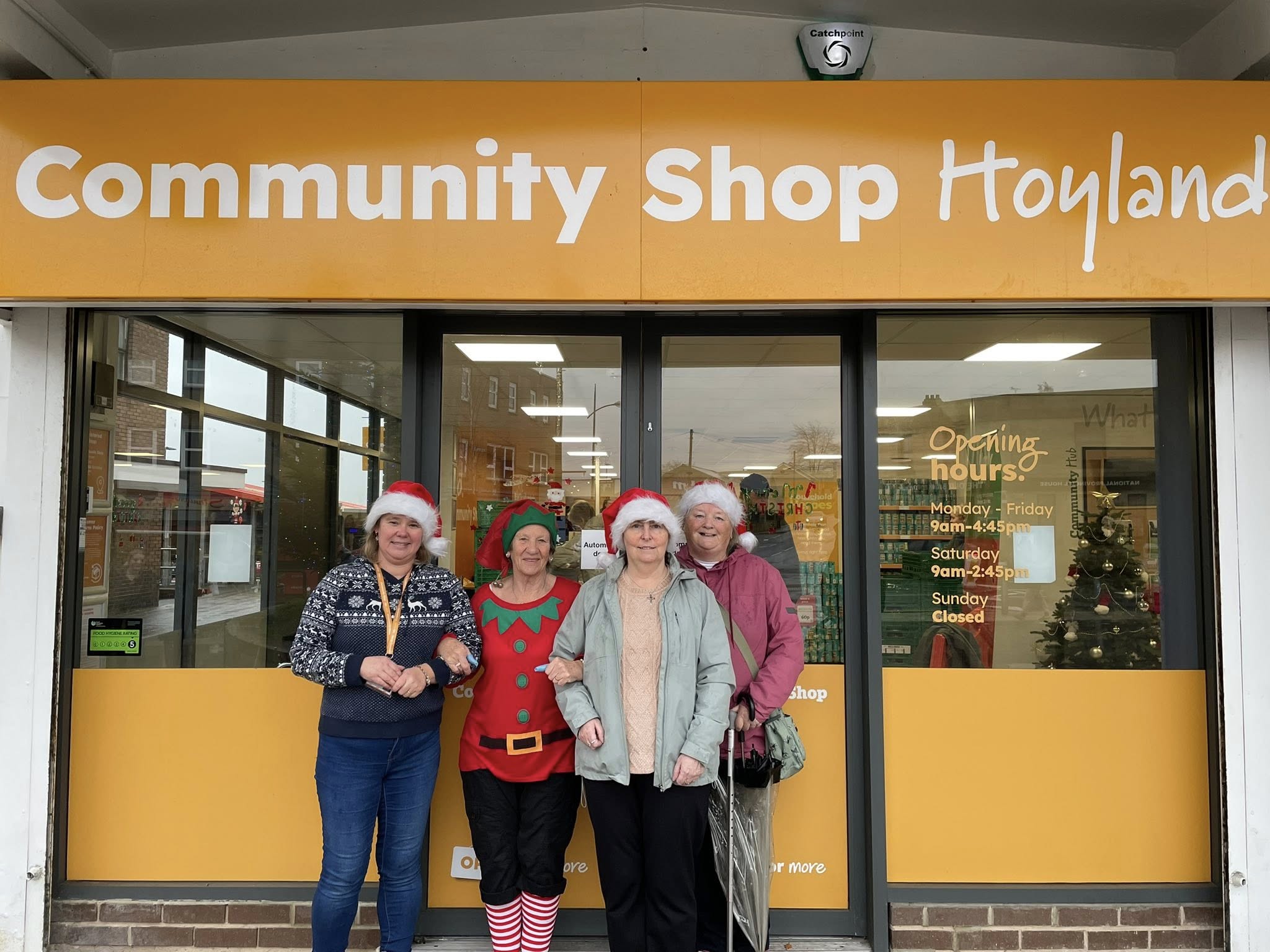 4 people stood outside the entrance of the Hoyland Community Shop in Santa hats
